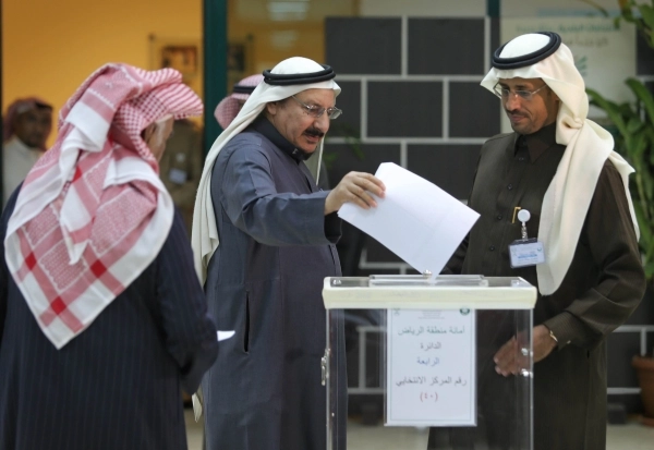 ناخب في الرياض يضع ورقة الاقتراع وسط متابعة من لجنة المركز (محمد مشهور)