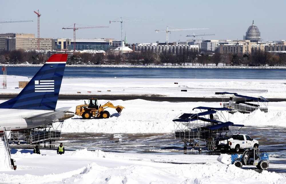 عمال أثناء إزالة الثلوج المتراكمة على مدرج مطار رونالد ريجان (أ ف ب)