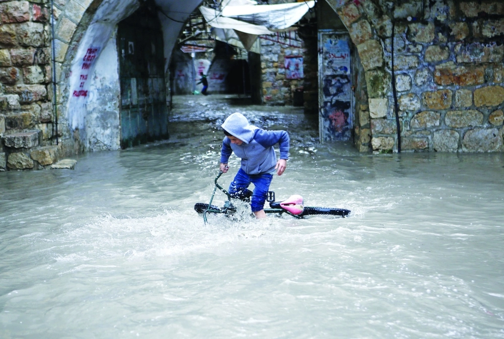 طفل فلسطيني يحاول ركوب دراجته بعد أمطار غزيرة في الخليل                (إ ب أ)