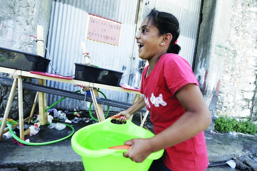 فتاة سورية تنقل ماء في مخيم قرب أثينا                                                                        (أ ف ب)