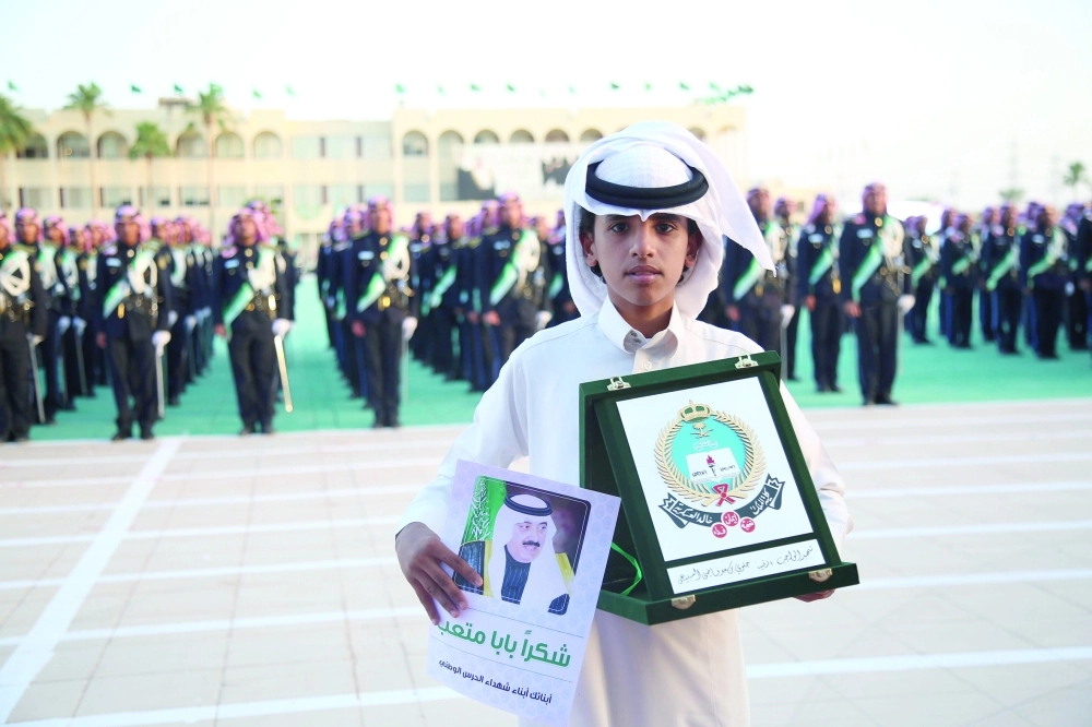 أحد أبناء شهداء الواجب حاملا درعا تكريميا لوالده في الرياض أمس (زياد الرزيزاء)