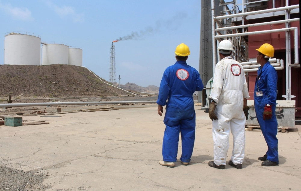 عمال يمنيون ينظرون إلى شعلة مصفاة عدن بعد إعادة تشغيلها (أ ف ب)