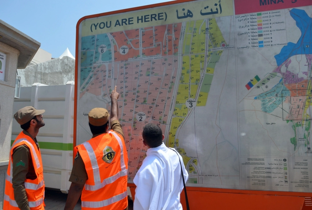 رجلا أمن يرشدان حاجا لمقصده أمام خريطة توضع الموقع في منى  (عبدالمحسن دومان)  