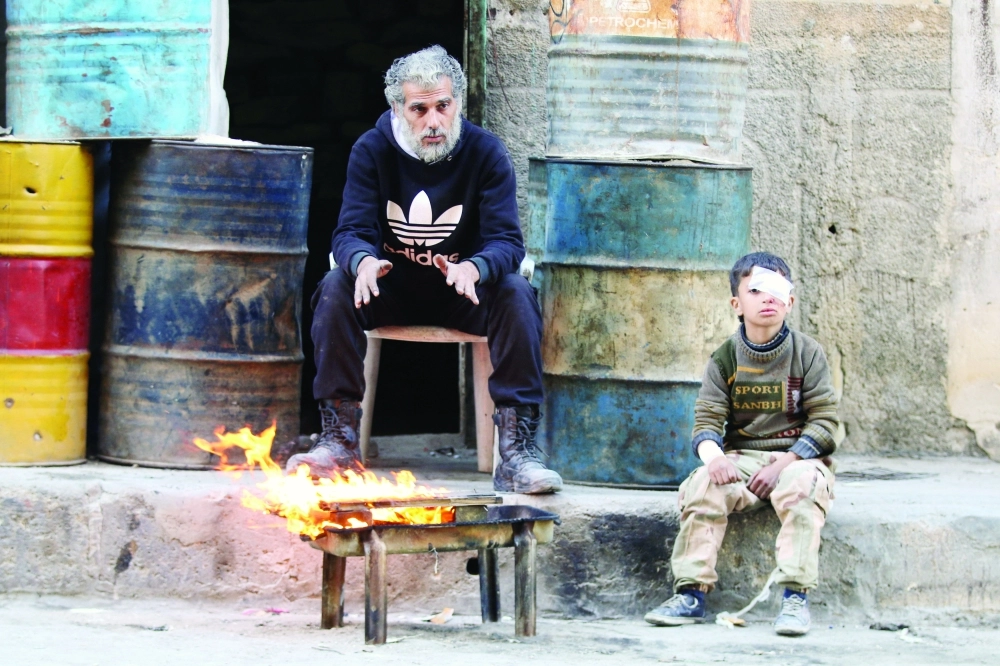 طفل مصاب ورجل يدفئان نفسيهما في مناطق المعارضة بحلب أمس(رويترز)