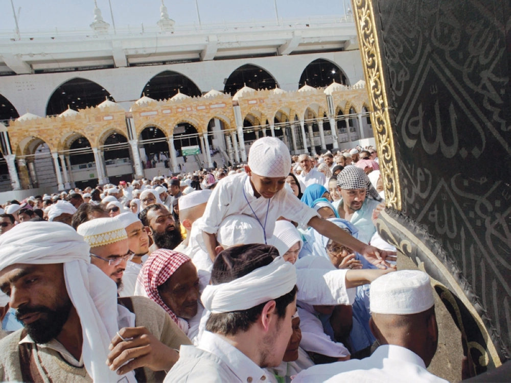 طفل على كتفي والده يحاول استلام الحجر الأسود (أ ف ب)