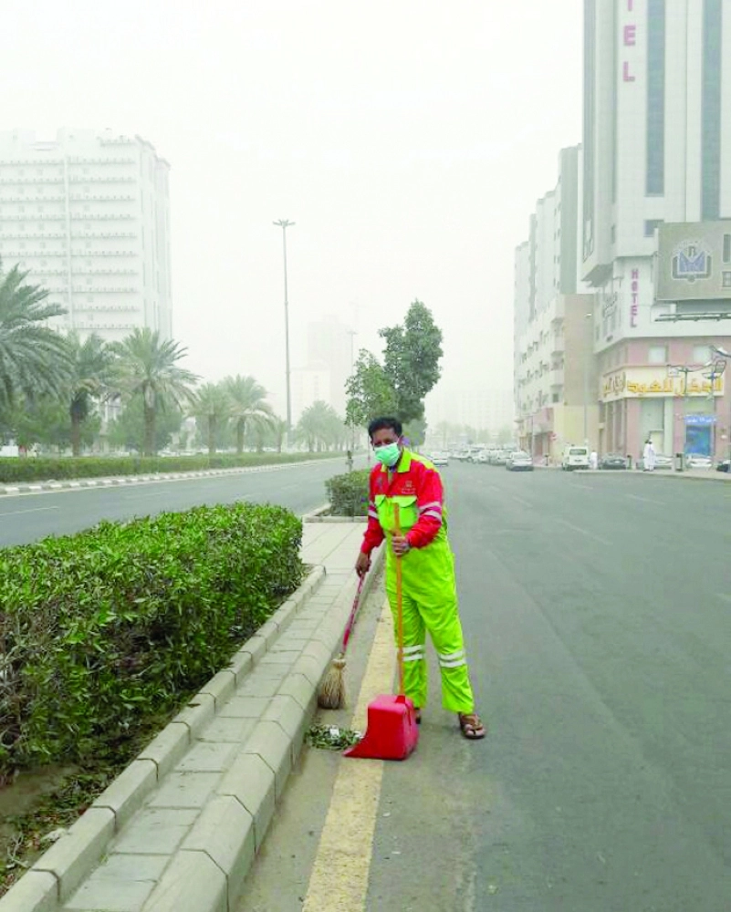 عامل نظافة في أحد شوارع مكة يرتدي كمامة لحمايته من الغبار