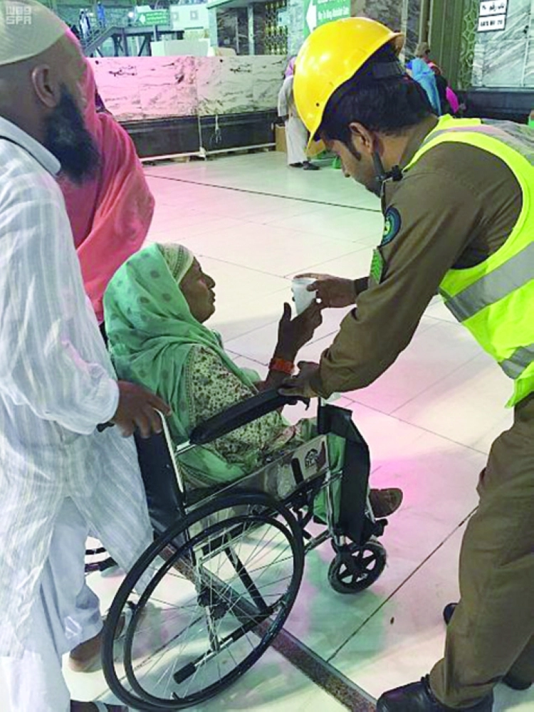 أحد أفراد الدفاع المدني يقدم الماء لمسنة في الحرم                        