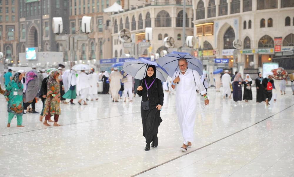 حجاج في ساحات الحرم المكي يحتمون بالمظلات من الأمطار أمس (واس)