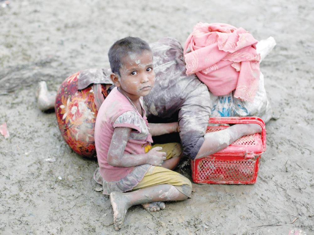 طفل يجلس بجوار أمه التي تستريح بعد عبورها الحدود إلى بنجلاديش أمس (رويترز)