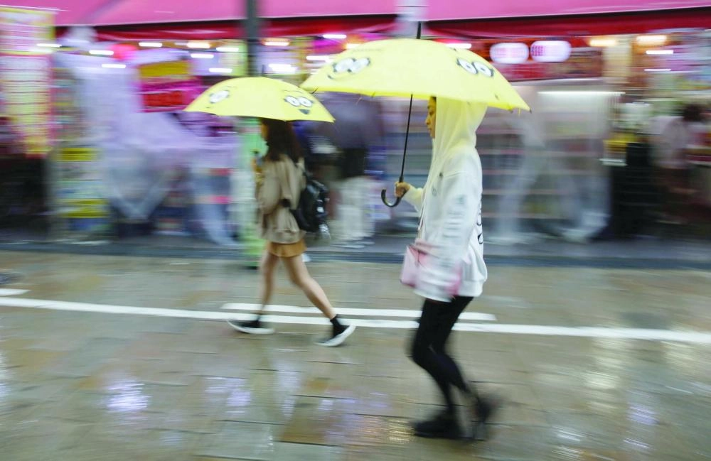 متسوقون تحت المظلات مع اقتراب إعصار لان من البر الرئيسي لليابان (رويترز)