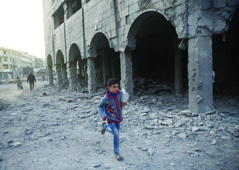 طفل سوري يجري وسط أطلال المباني في مدينة دوما (رويترز)