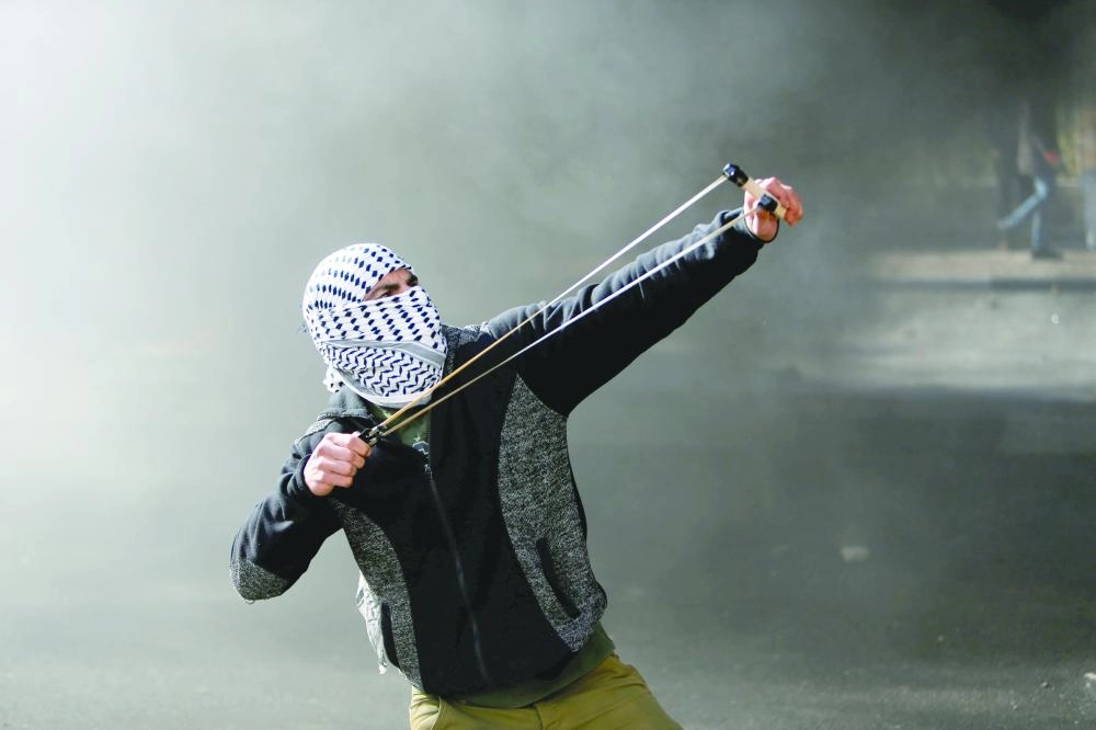 A Palestinian protester uses a sling shot to hurl stones towards Israeli troops during clashes in the West Bank city of Bethlehem