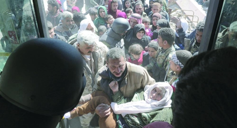 رجل يحمل والدته وخلفه عشرات المدنيين لحظة مغادرتهم الغوطة الشرقية                                                                               (إ ب أ)