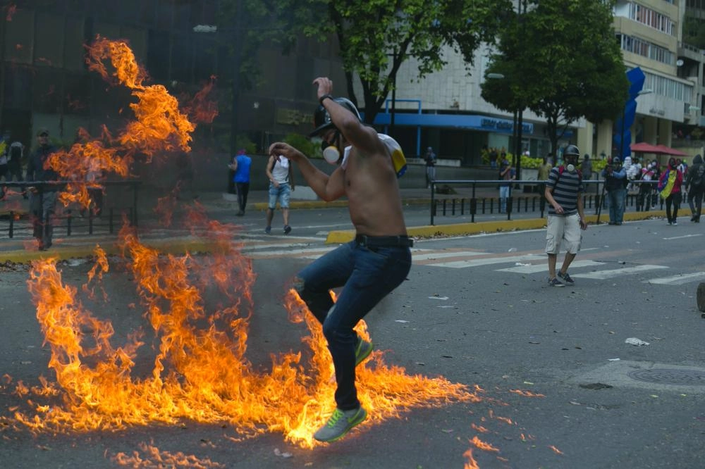 23 January 2019, Venezuela, Caracas: A protester jumps on fire during clashes with Riot Police at mass protests against Venezuelan President Nicolas Maduro and in support of Juan Guaido, the head of Venezuela's opposition-dominated National Assembly, who has declared himself interim president. Maduro ordered the termination of diplomatic relations with the USA on Wednesday, after the US earlier shifted its recognition to Juan Guaido of the opposition. Photo: Rafael Hernandez/dpa