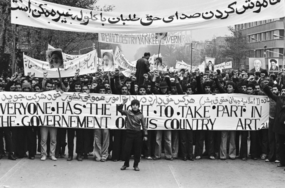An Iranian boy, fist raised in symbolic defiance, heads a huge crowd of Ayatollah Khomeini supporters across Tehran in an anti-Shah demonstration estimated at over a million strong, Dec. 10, 1978.  Behind him demonstrators carry a banner reading "Everyone has the right to take part in the government of his own country," and behind another reads "We will destroy Yankee power in Iran." (AP Photo)