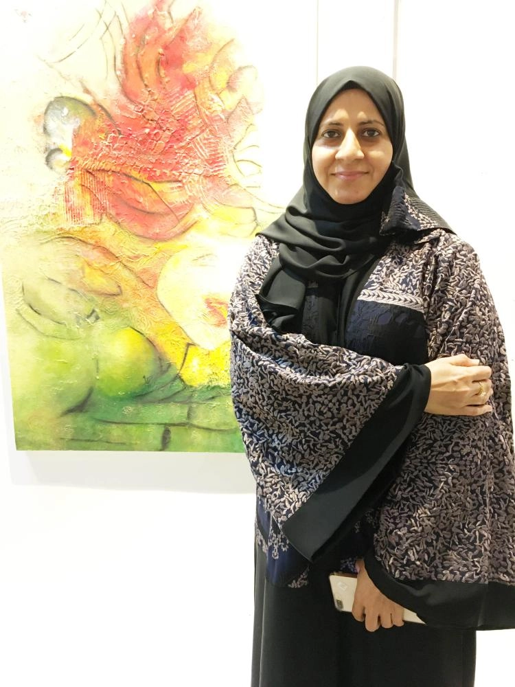 الفنانة زينب آل يوسف أمام إحدى لوحاتها في المعرض (مكة)