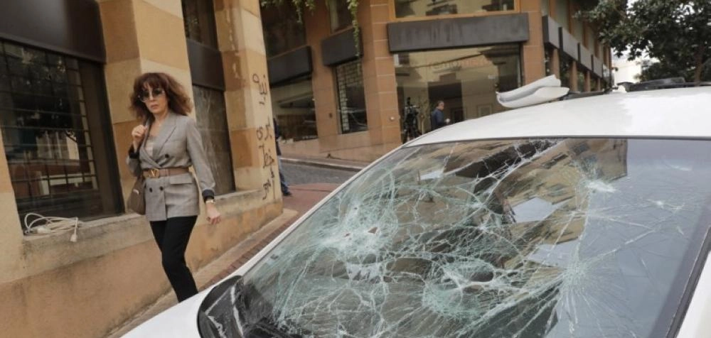 سيدة تنظر إلى سيارة حطم زجاجها خلال مظاهرات لبنان      (أ ف ب)