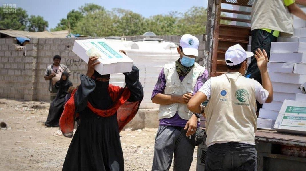 سيدة تحمل كرتون تمور وفريق المركز يتأهب للتوزيع (واس)