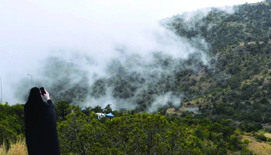 سيدة خلال توثيقها الضباب من على قمم جبال عسير 