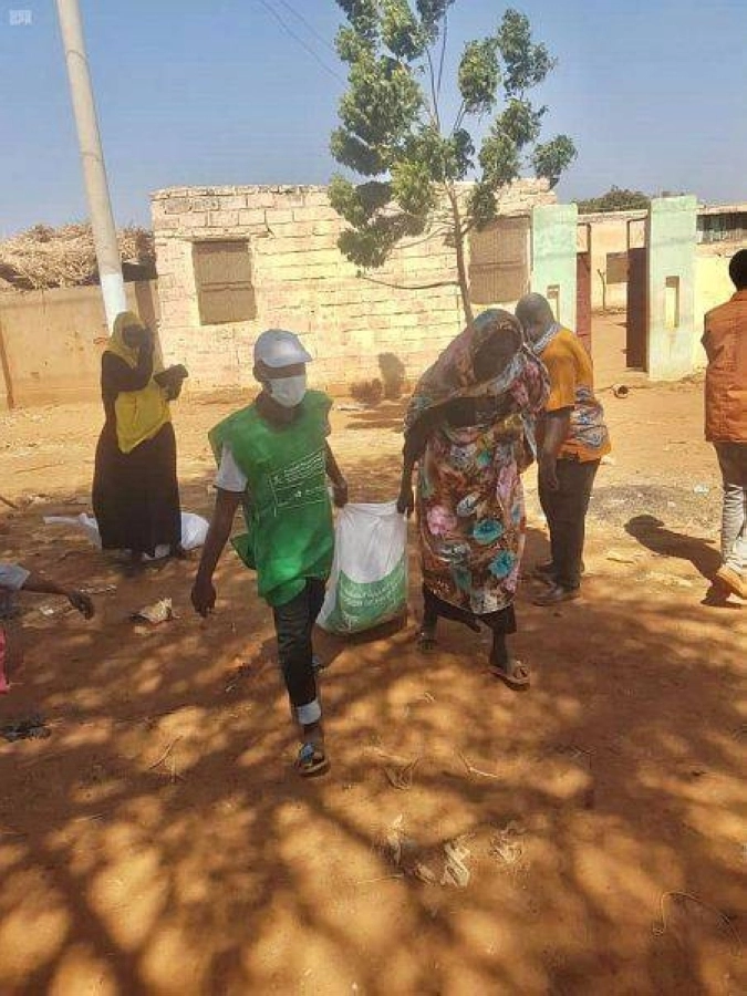 متطوع يساعد سودانية في حمل السلة (واس)