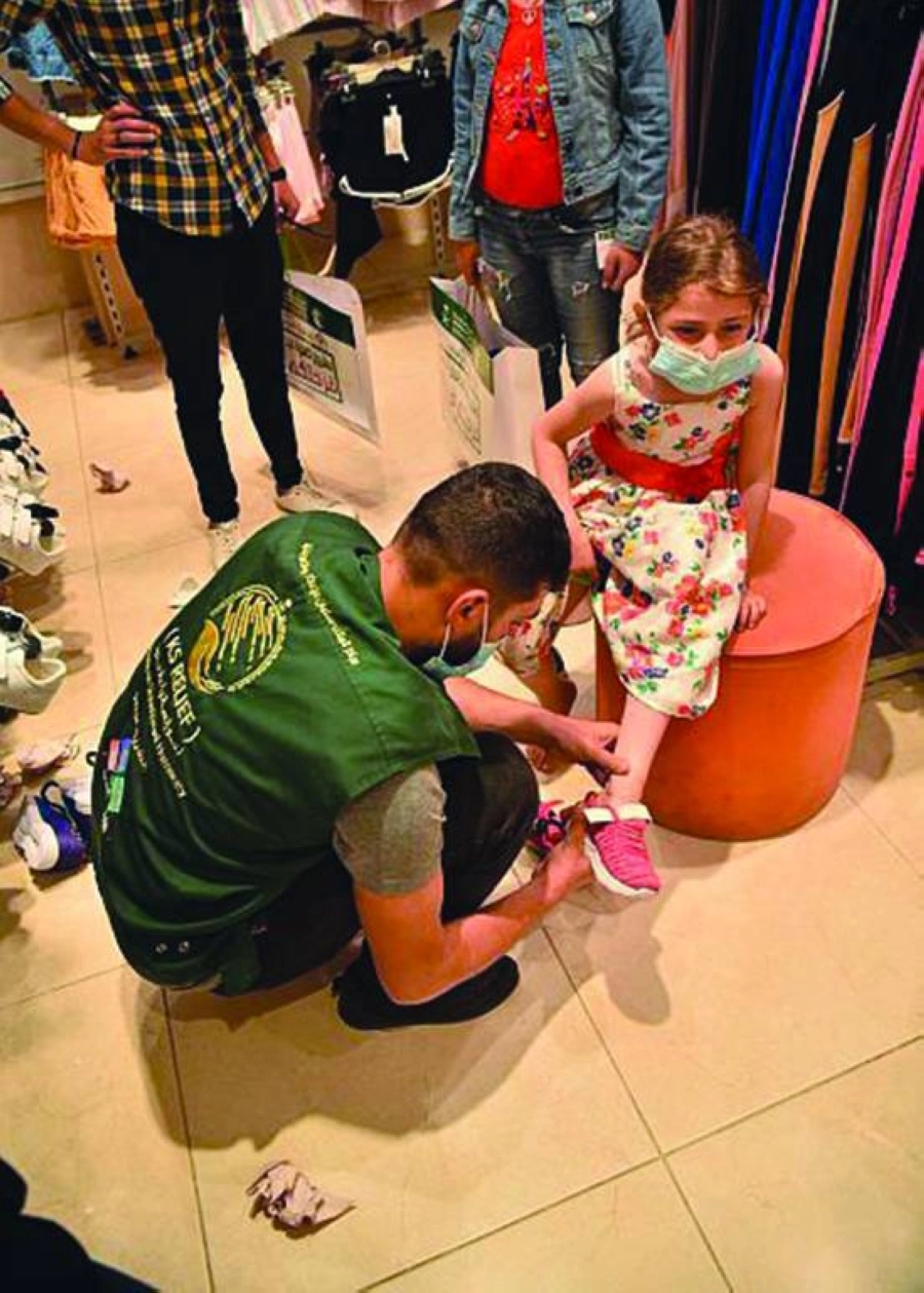 أحد أفراد المركز يساعد طفلة سورية في ارتداء حذائها  (واس)