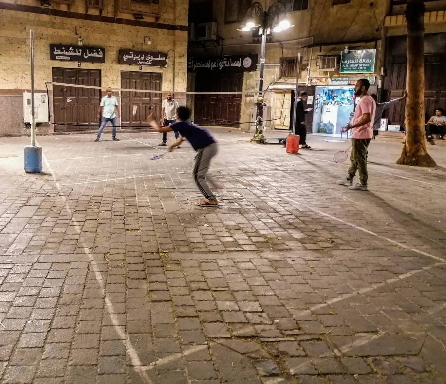 عمالة تحول ساحة من ساحات الخاسكية في جدة لملعب تنس بعد الانتهاء من أعمالهم ليلا، مما يشد انتباه المارة من المتسوقين
