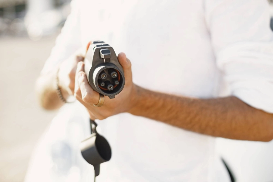 Young adult man standing near electric car with socket