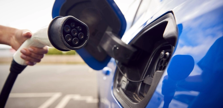 Close Up Of Hand Attaching Charging Cable To Environmentally Friendly Zero Emission Electric Car