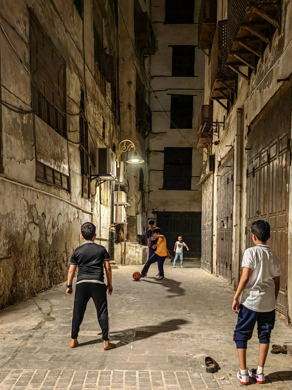 أطفال يلعبون مباراة كرة قدم في وقت متأخر من الليل بين أزقة تاريخية جدة. 