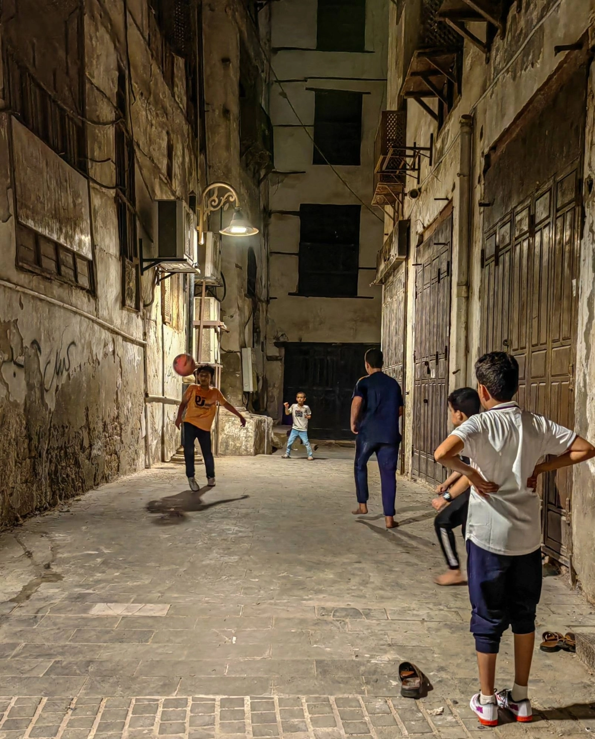 أطفال يلعبون مباراة كرة قدم في وقت متأخر من الليل بين أزقة تاريخية جدة. 