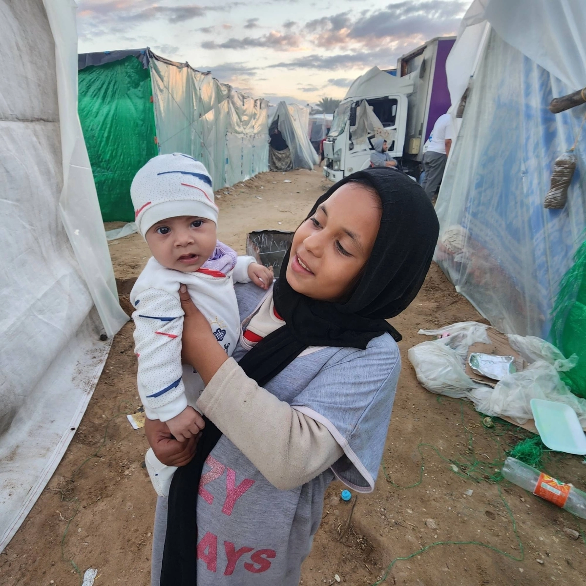 


طفلة تحمل أختها في مخيم النازحين 