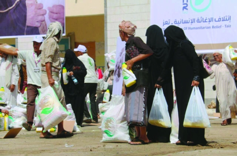 يمنيون يحملون سلالا غذائية يوزعها مركز الملك سلمان، في تعز (واس)