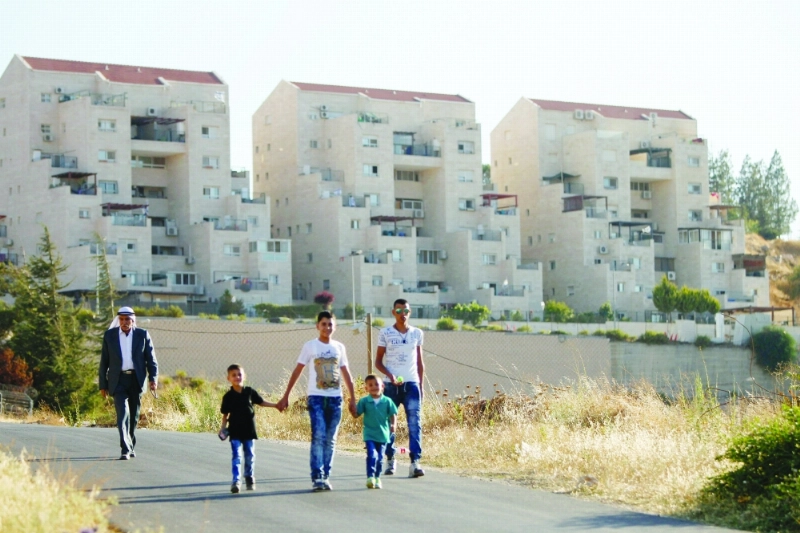 فلسطينيون يسيرون أمام وحدات استيطانية في الخليل (أ ف ب)