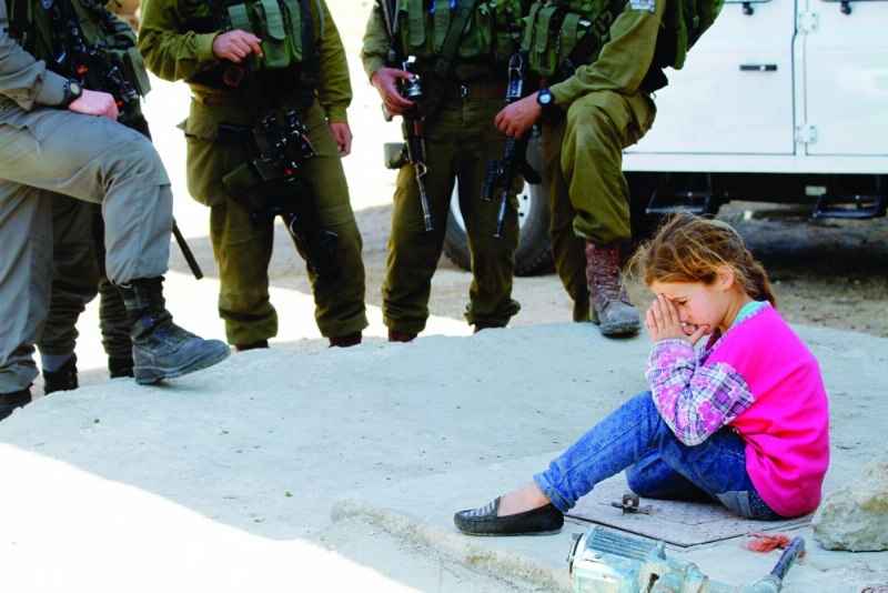طفلة فلسطينية تجلس أمام منزلها بنابلس فيما يتابعها جنود الاحتلال (إ ب أ)