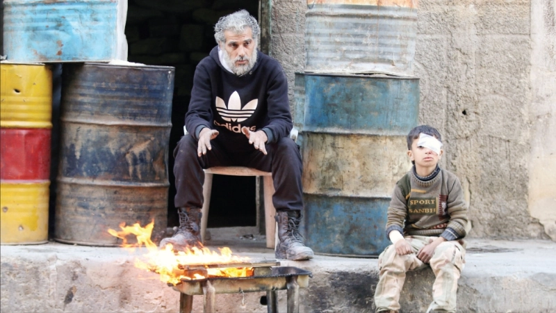 طفل مصاب ورجل يدفئان نفسيهما في مناطق المعارضة بحلب أمس (رويترز)