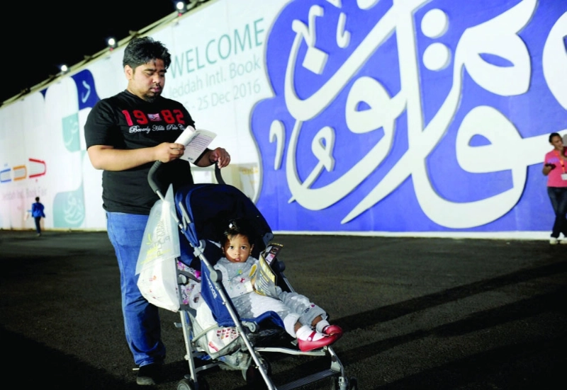يدفع طفلته ويطالع كتابه على باب المعرض