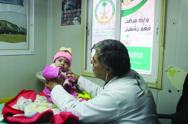 طبيب يفحص طفلا سوريا بالعيادات السعودية (واس)