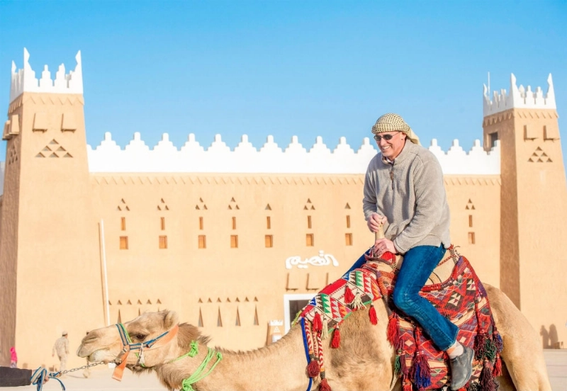 زائر أجنبي يمتطي جملا في جناح القصيم (واس)