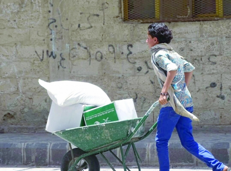 صبي يمني بتعز يدفع عربة تحمل سلالا غذائية سعودية
