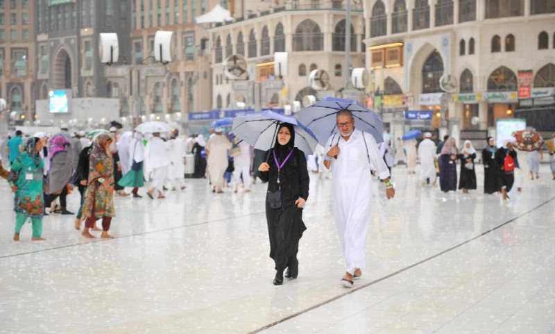 حجاج في ساحات الحرم المكي يحتمون بالمظلات من الأمطار أمس (واس)
