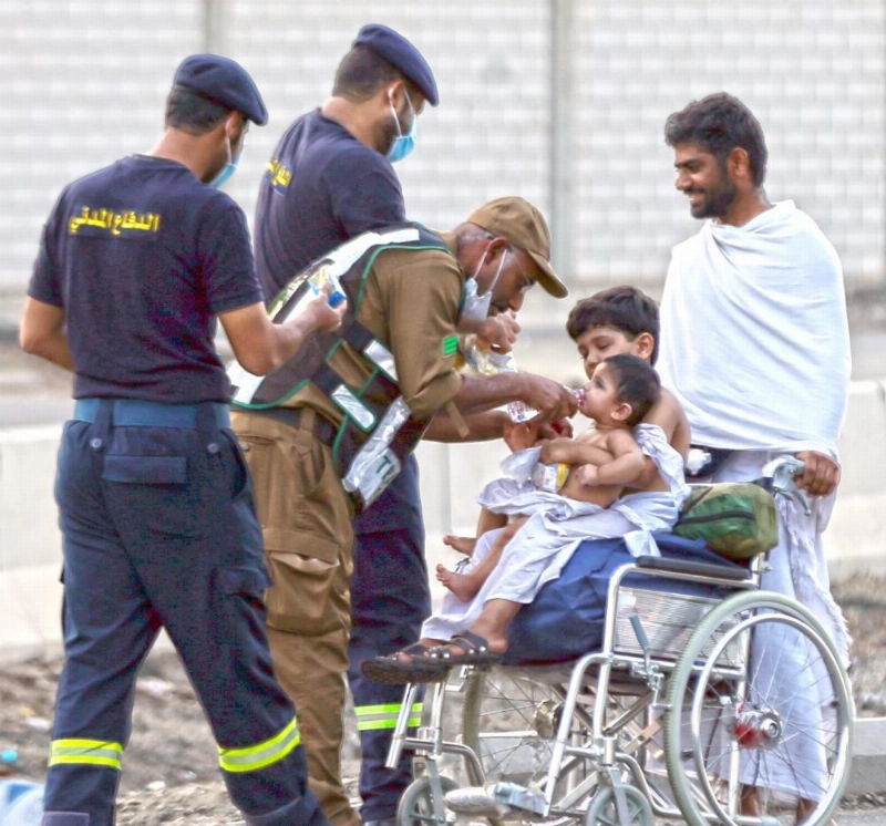 أحد أفراد قوات الحج يسقي طفلا الماء في الموسم الماضي (عبدالمحسن دومان)