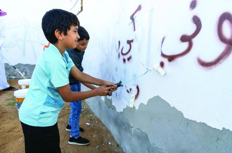 طفلان يشاركان في إزالة كتابات على أحد الجدران في تبوك
