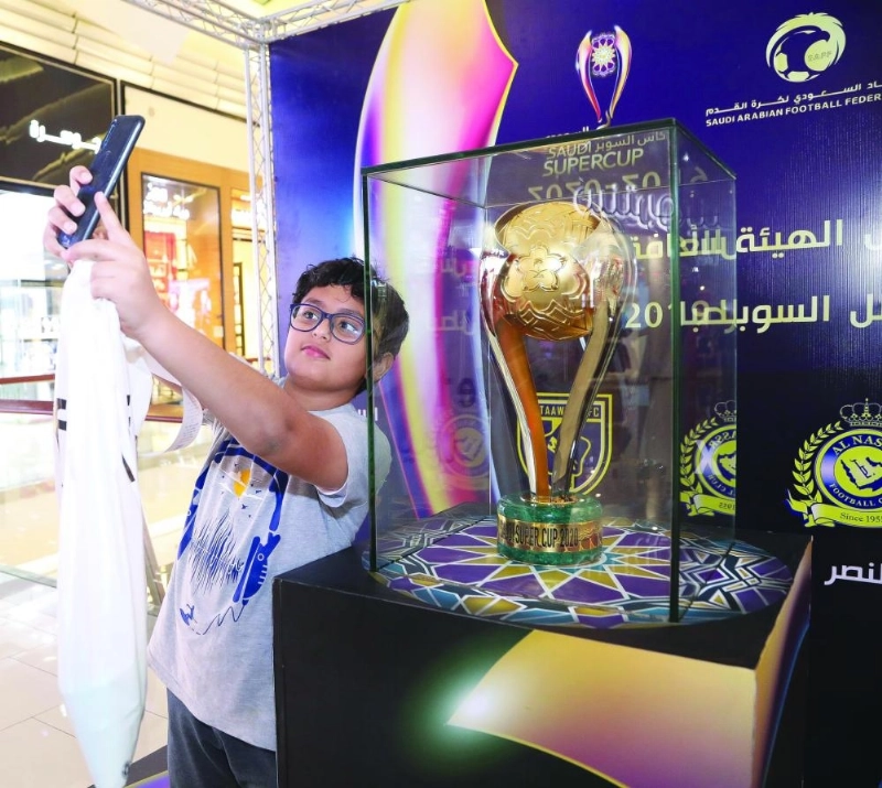 مشجع ومشجعة يلتقطان صورا تذكارية مع كأس البطولة في مول بجدة (هيئة الرياضة)
