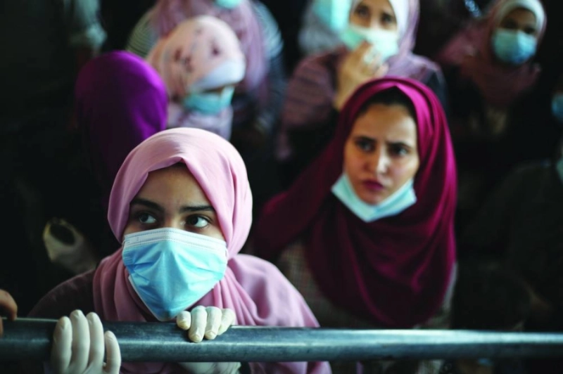 فلسطينيون يرتدون أقنعة وجه في انتظار عبور معبر رفح إلى مصر (د ب أ)
