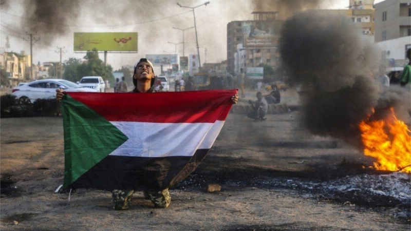 سوداني يحمل علم بلاده وسط الفوضى والدمار (مكة)