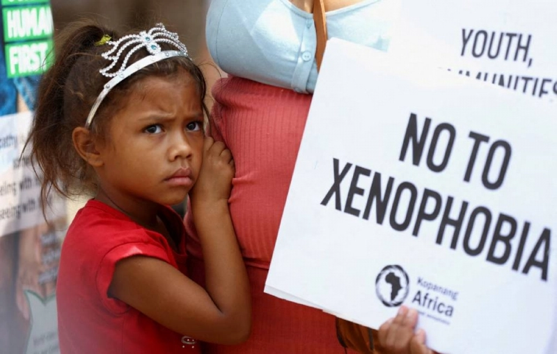 FILE PHOTO: A child looks on next to her mother holding a placard, during a march by a South African anti-xenophobia group following a recent campaign by another group which called on the government to prioritise jobs for nationals and remove undocumented immigrants from the country, in Hillbrow, Johannesburg, South Africa, March 26, 2022. REUTERS/ Siphiwe Sibeko/File Photo FILE PHOTO: A child looks on next to her mother holding a placard, during a march by a South African anti-xenophobia group following a recent campaign by another group which called on the government to prioritise jobs for nationals and remove undocumented immigrants from the country, in Hillbrow, Johannesburg, South Africa, March 26, 2022. REUTERS/ Siphiwe Sibeko/File Photo