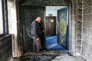 A man inspects the burnt-out entrance to the Abu Bakr as-Siddiq Mosque near the village of Tal, west of Nablus, on Monday.