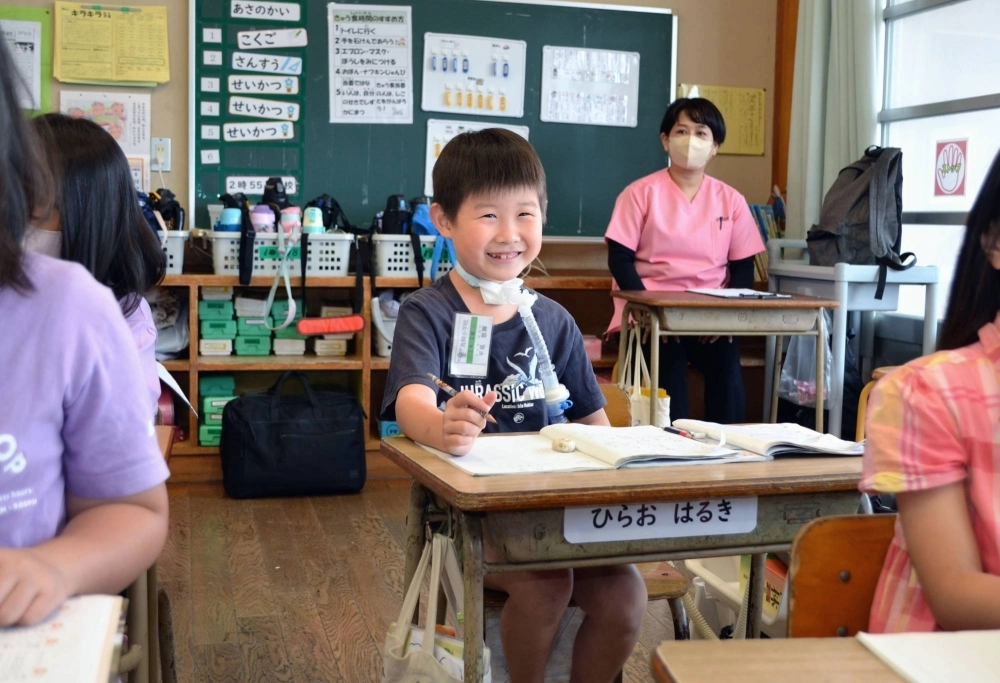 Haruki Hirao, second grader at Torikai Elementary School in Kurume, Fukuoka Prefecture, attends a mathematics class in May as nurse Yoshimi Yoshiyama looks on from the back of the classroom. Haruki Hirao, second grader at Torikai Elementary School in Kurume, Fukuoka Prefecture, attends a mathematics class in May as nurse Yoshimi Yoshiyama looks on from the back of the classroom.