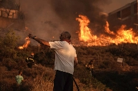 Firefighters and volunteers work to extinguish a burning field during a wildfire in Saronida, south of Athens, Greece, on July 17. | Bloomberg