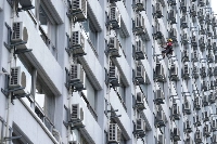 A worker washes windows next to air conditioning units at an apartment building in Tokyo on July 21. | Bloomberg
